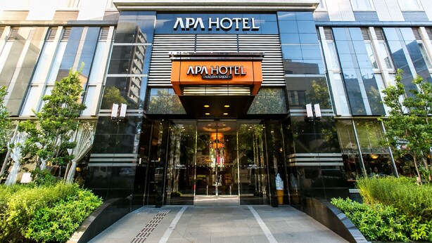 The APA Hotel entrance with a modern facade, large glass windows, and a prominent sign.