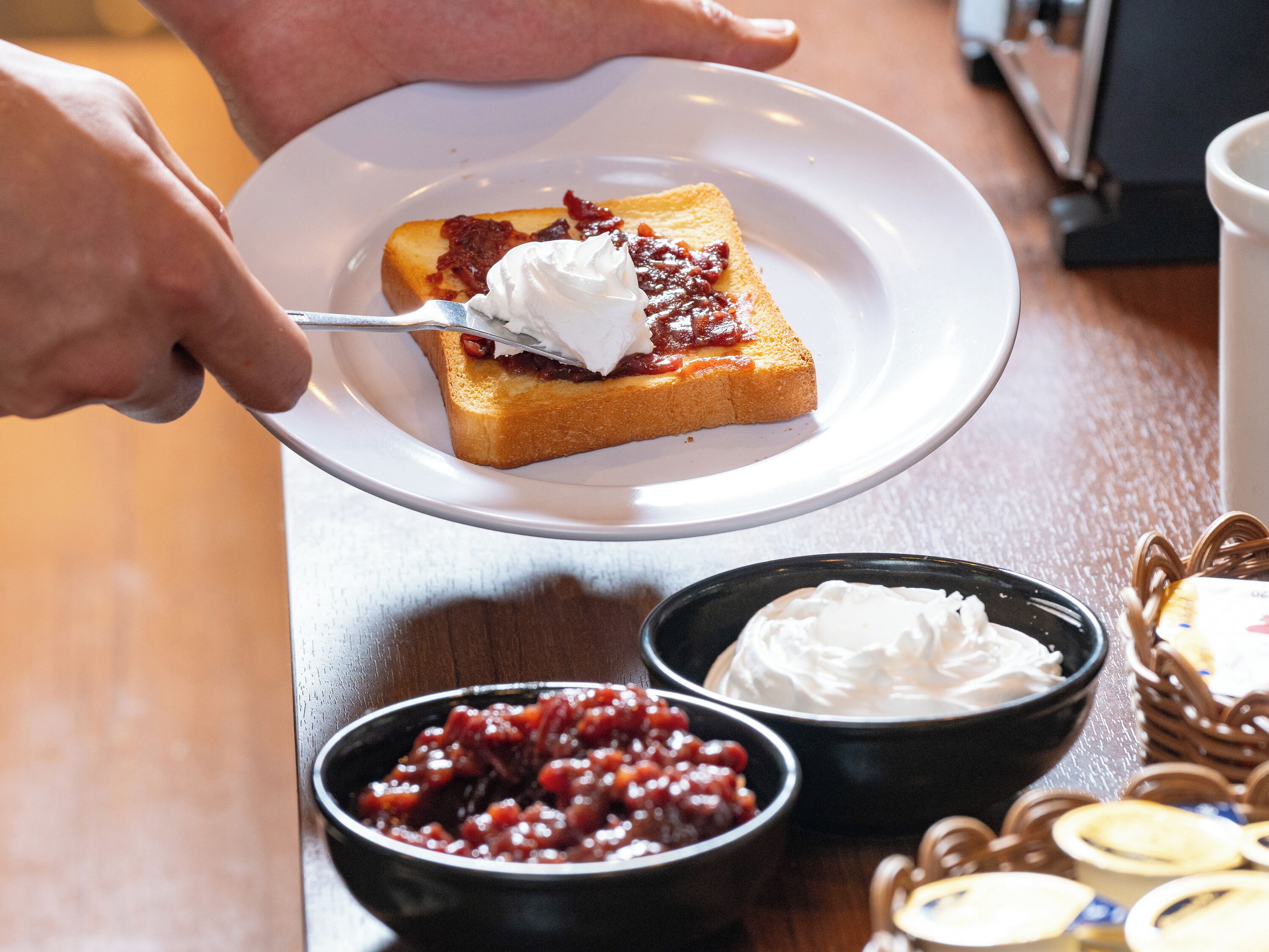 A slice of toast with jam and whipped cream on a plate.