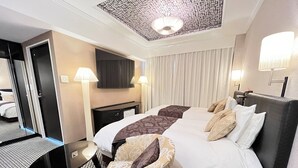A hotel room with a large bed, two bedside tables, a desk, a chair, a TV, and a patterned ceiling.