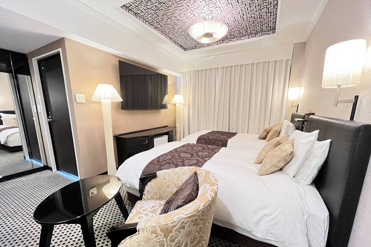 Een hotelkamer met een groot bed, twee nachtkastjes, een bureau, een stoel, een televisie en een kamerplafond met een patroon.