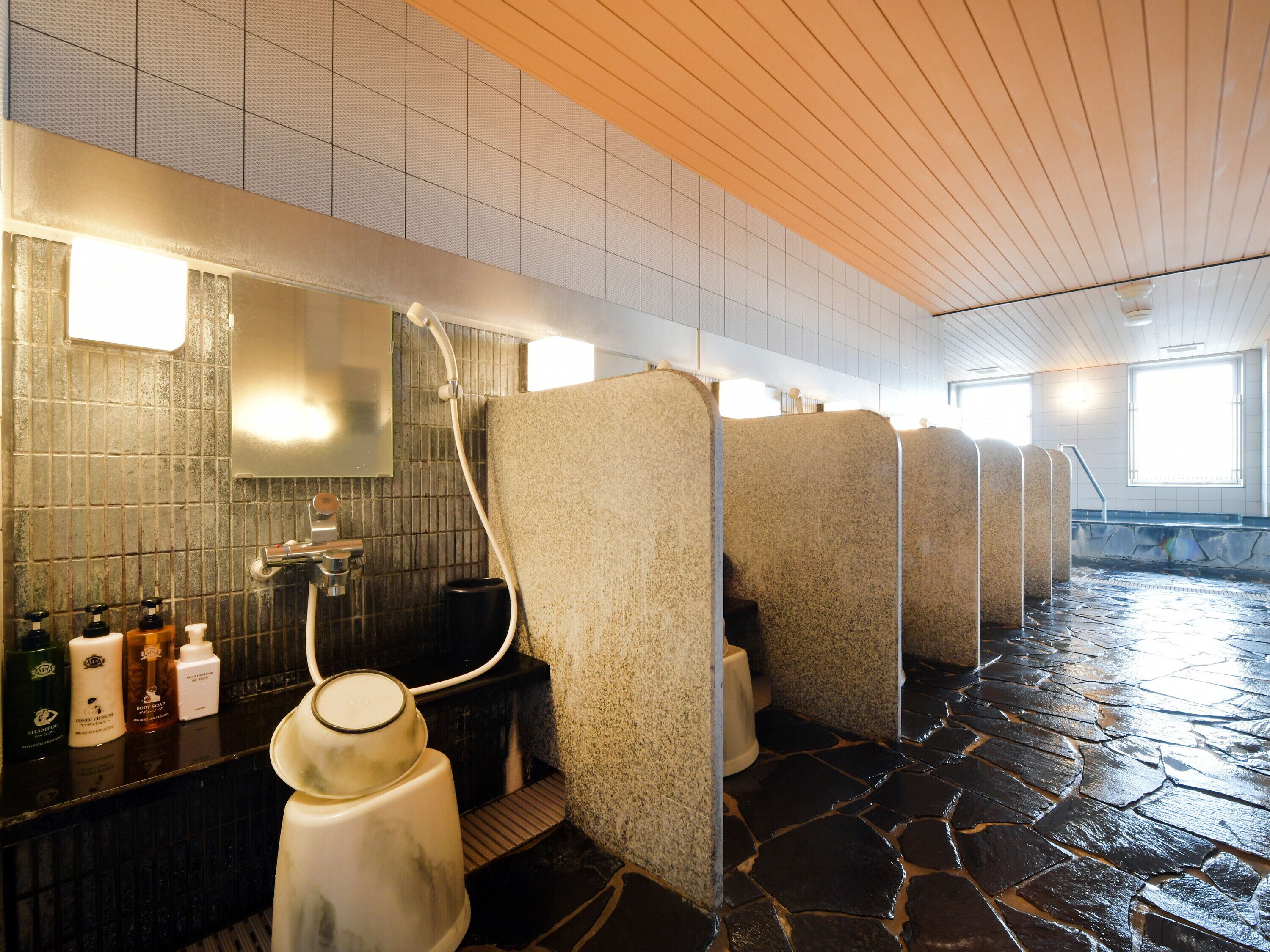 Ein modernes Badezimmer mit Steinböden, einem großen Spiegel und einer Reihe separater Duschkabinen.
