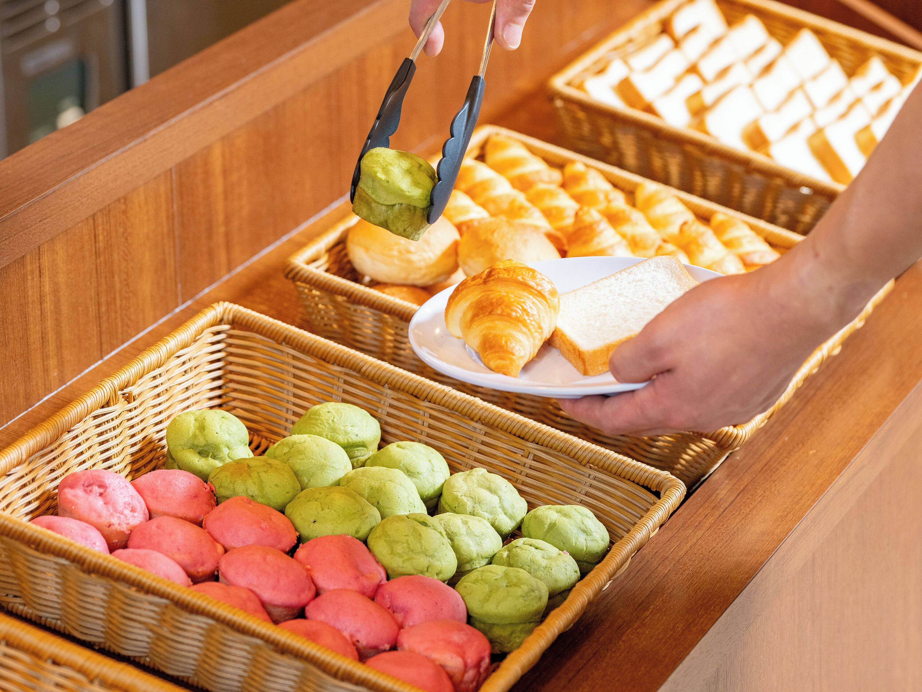 Een buffet met diverse gebakken producten, waaronder brood, croissants en gebakjes in rieten manden.