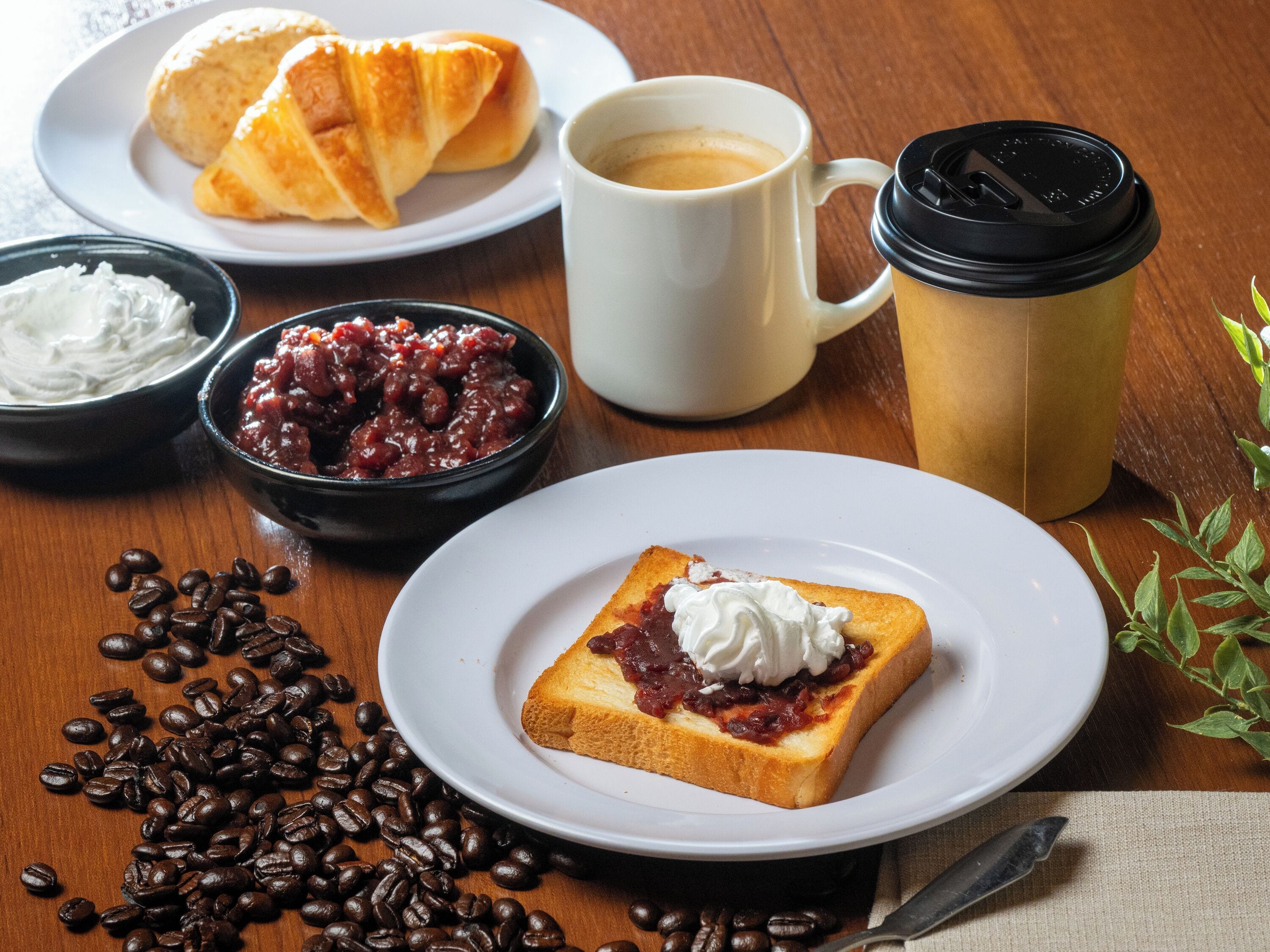 A breakfast setting with croissants, coffee, and a slice of toast with jam and whipped cream.