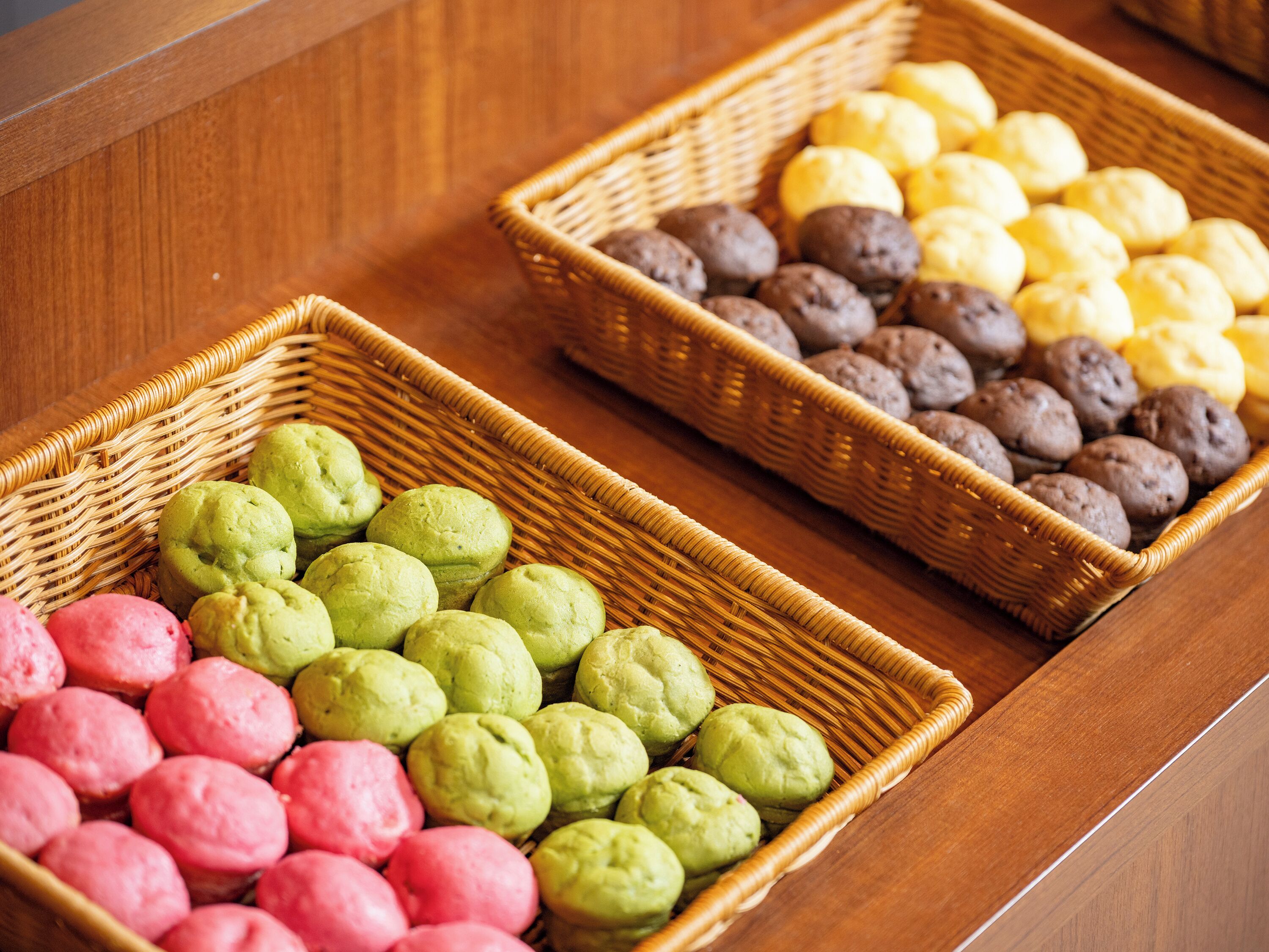 Two wicker baskets filled with colorful pastries on a wooden surface.