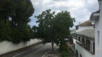 Una calle con un edificio blanco a la derecha, un árbol en el centro y un coche estacionado en primer plano.