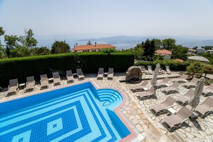 A swimming pool with a geometric tile pattern, surrounded by lounge chairs and umbrellas, with a view of distant mountains and houses.