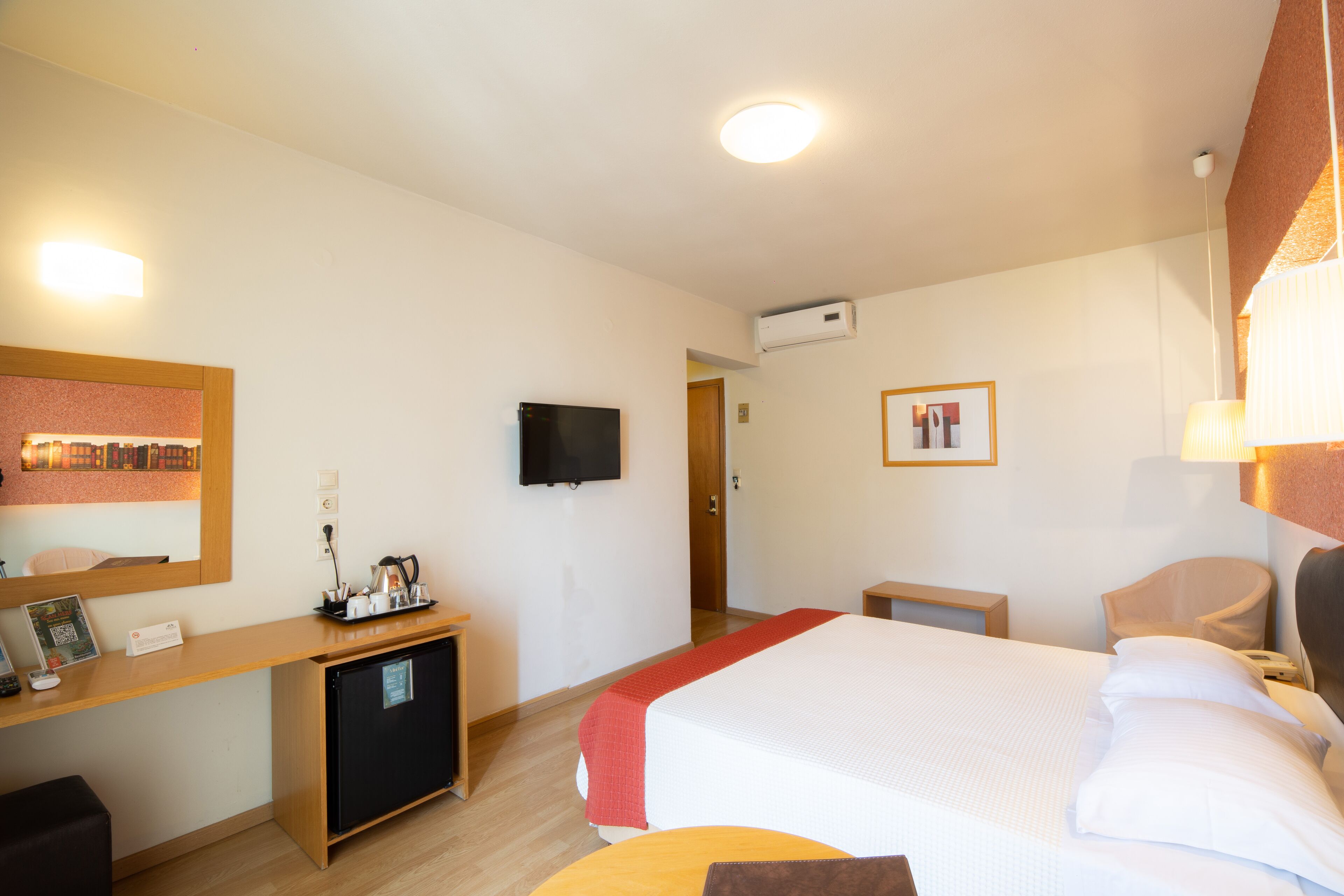A hotel room with a bed, a desk with a computer, a television, and a small refrigerator.