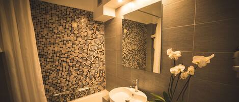 A modern bathroom with a mosaic tile wall, a round sink, a mirror, and a potted orchid.