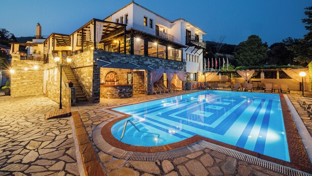 A large outdoor swimming pool with a stone deck, a two-story building with balconies, and a stone staircase leading to the upper level. - Portaria Hotel (Volos)