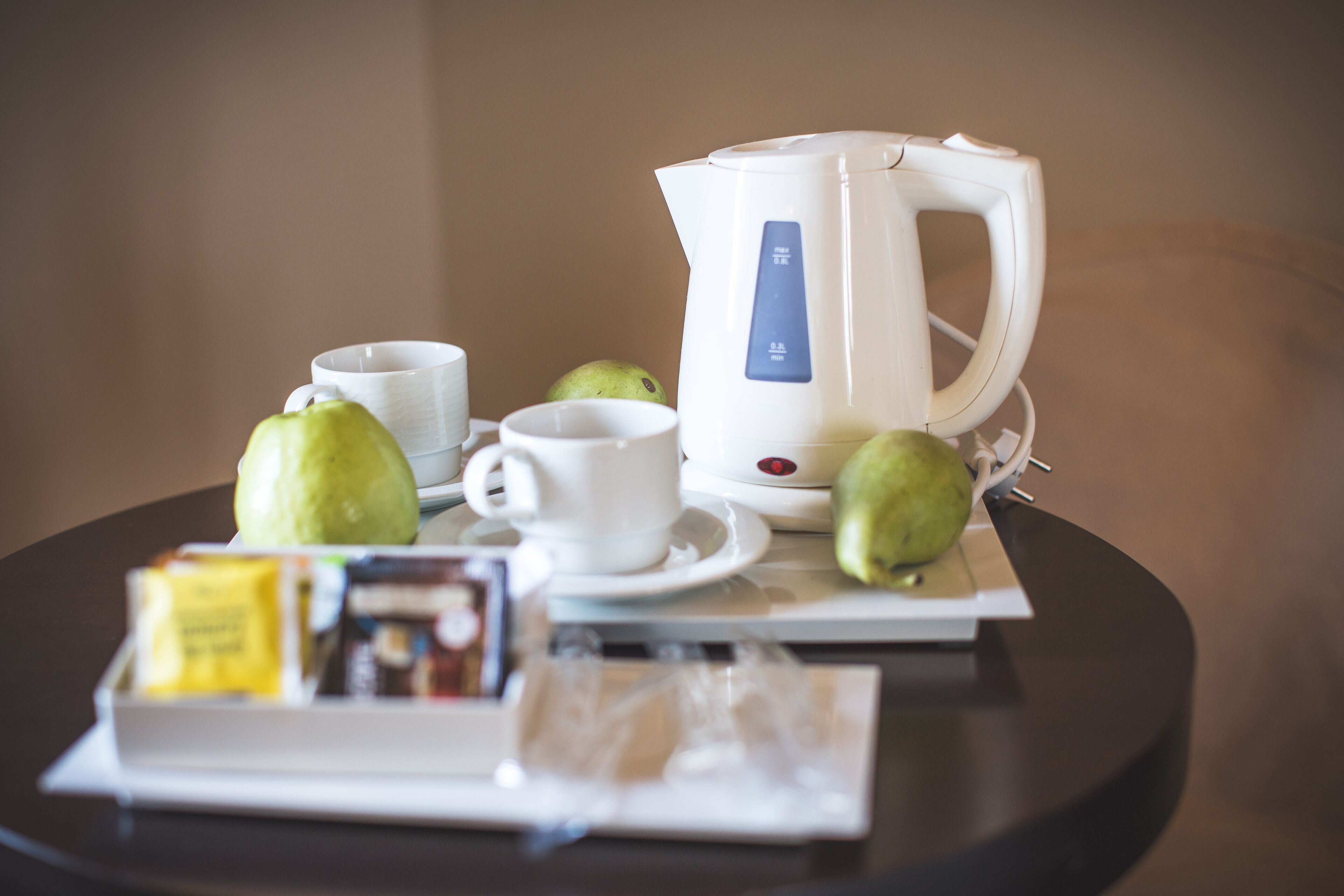 Una mesa con un hervidor eléctrico blanco, dos tazas blancas y dos manzanas verdes.