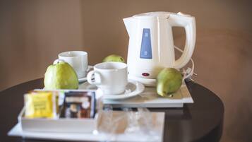 Una mesa con un hervidor eléctrico blanco, dos tazas blancas y dos manzanas verdes.