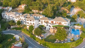 A hotel with multiple white buildings, a swimming pool, and a well-maintained garden. - Portaria Hotel (Volos)