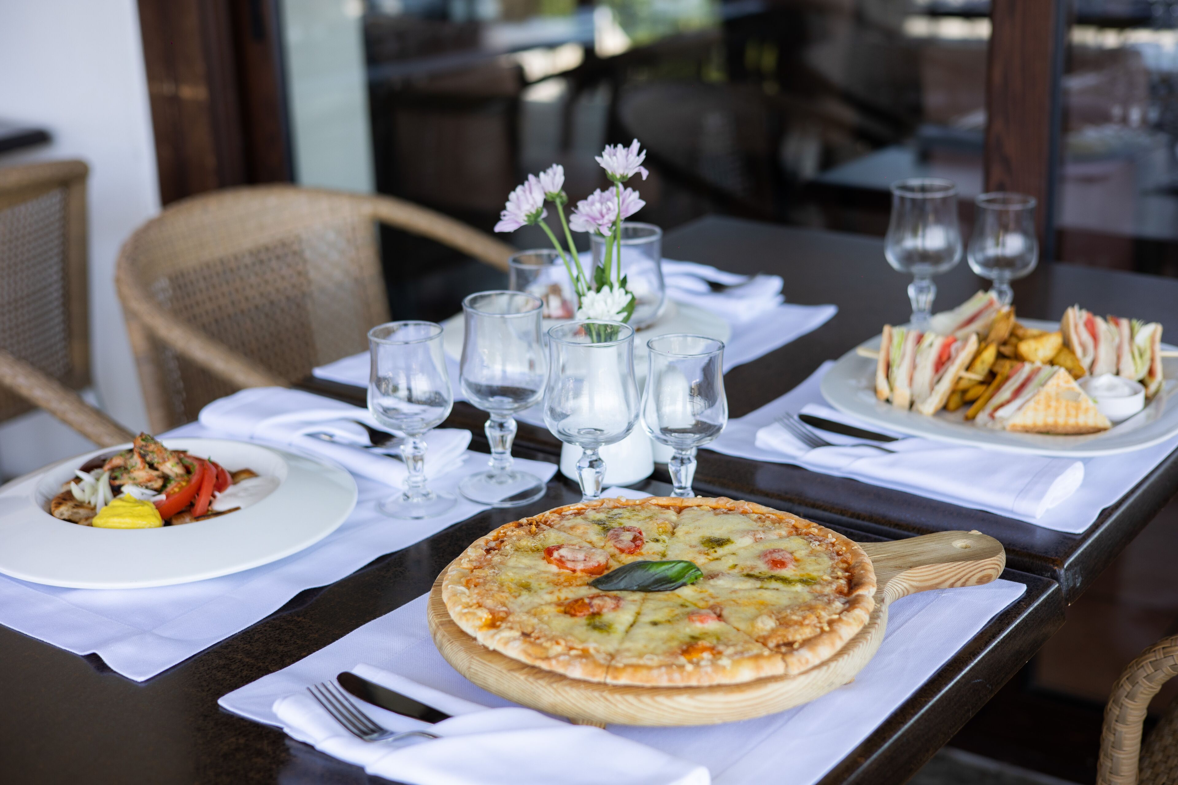 A dining table with a pizza, a plate of sandwiches, and a glass of water.