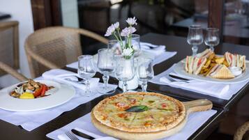 A dining table with a pizza, a plate of sandwiches, and a glass of water.