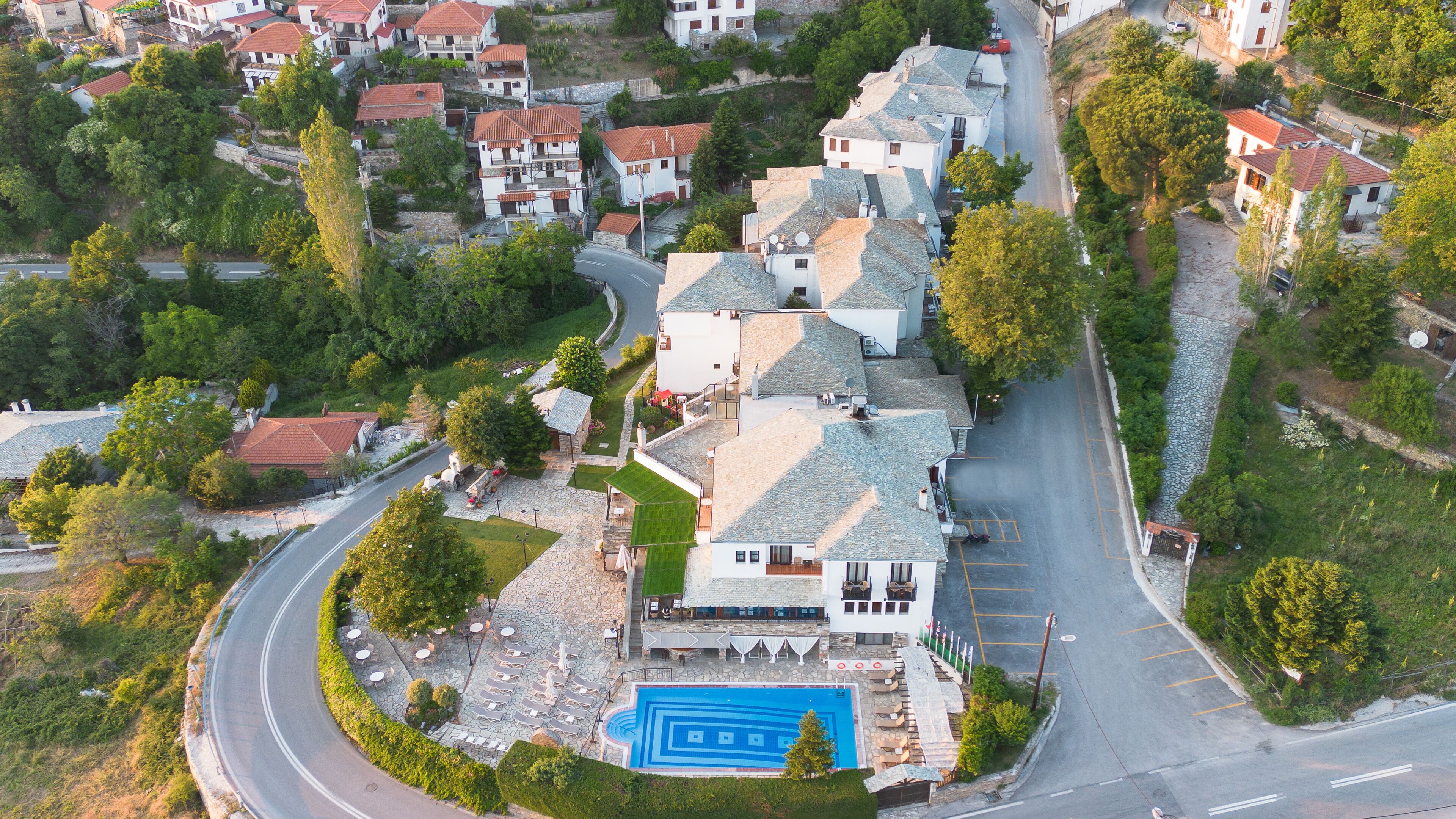 Vista aérea de una zona residencial con una casa destacada, piscina, abundante vegetación y una carretera sinuosa.