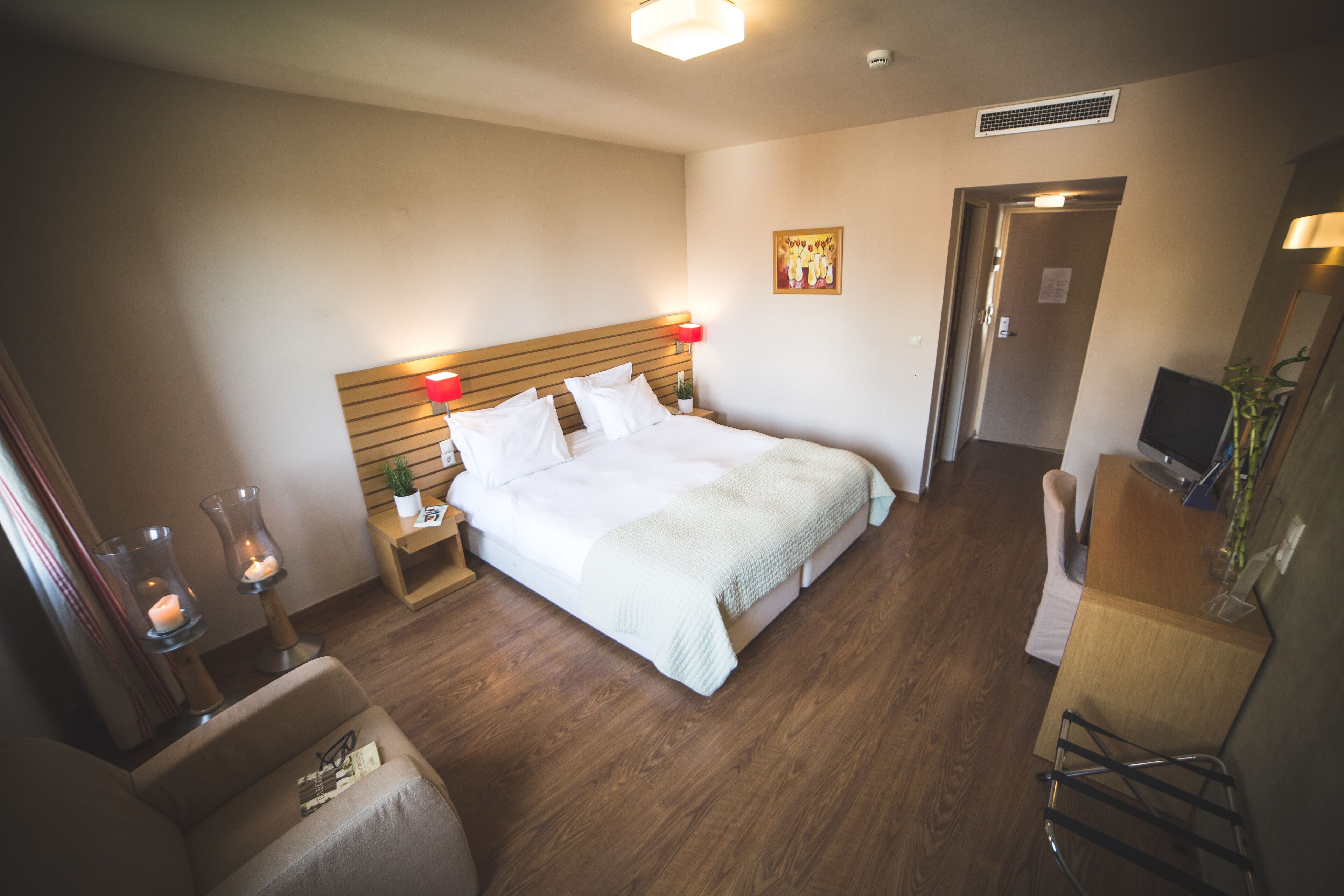 A hotel room with a large bed, bedside lamps, a small table with a candle, a chair, and a desk with a computer.