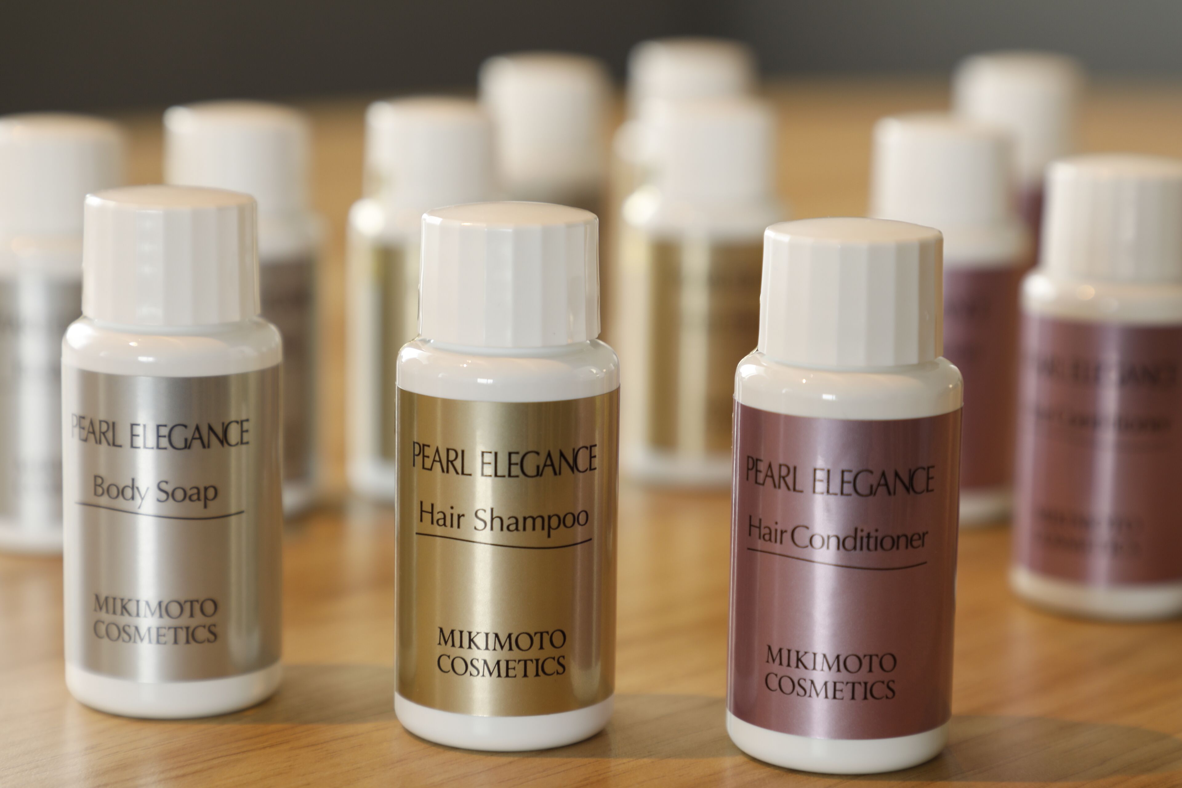 Three bottles of Pearl Elegance body soap, hair shampoo, and hair conditioner on a wooden surface.