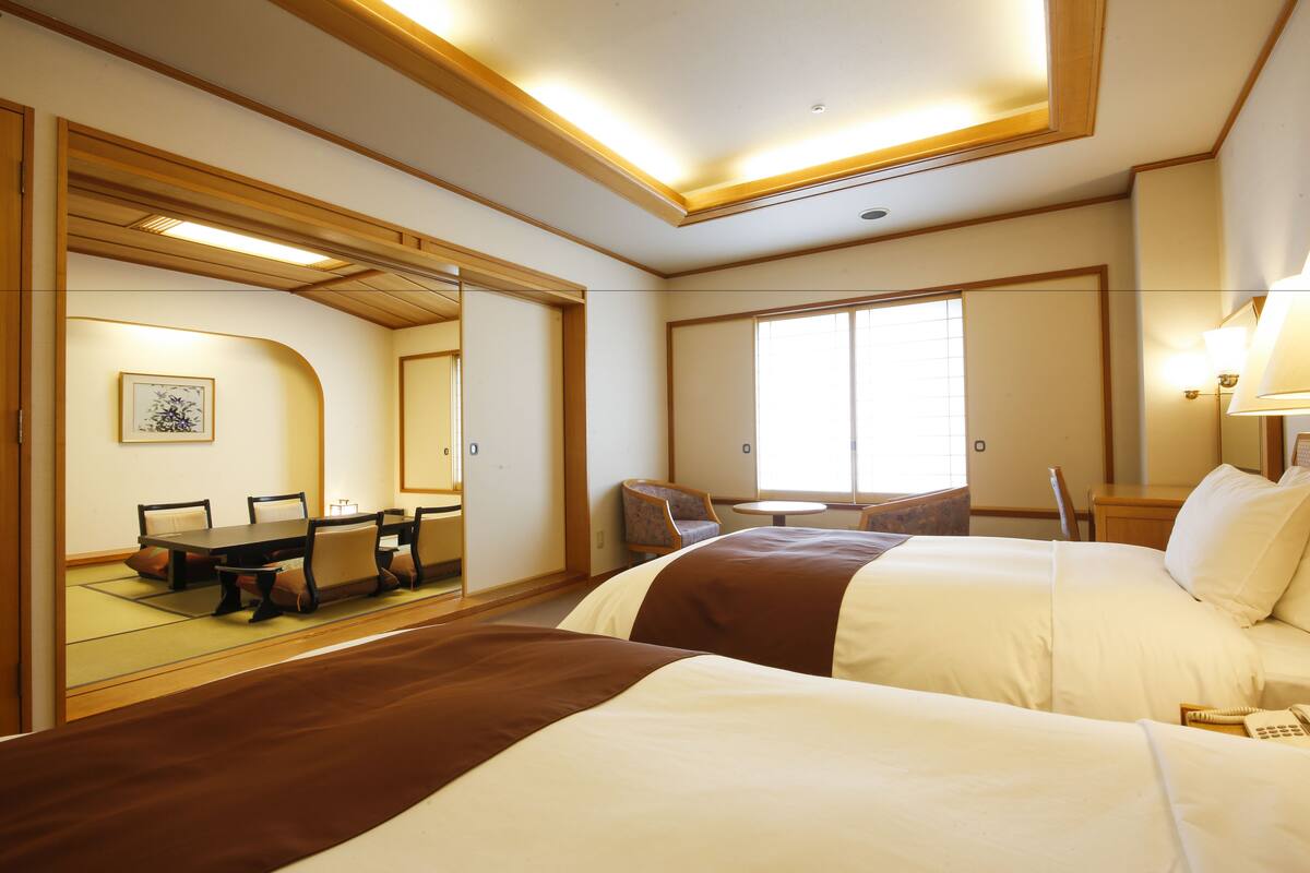 A hotel room with two beds, a dining table with chairs, a small table, and a large mirror.