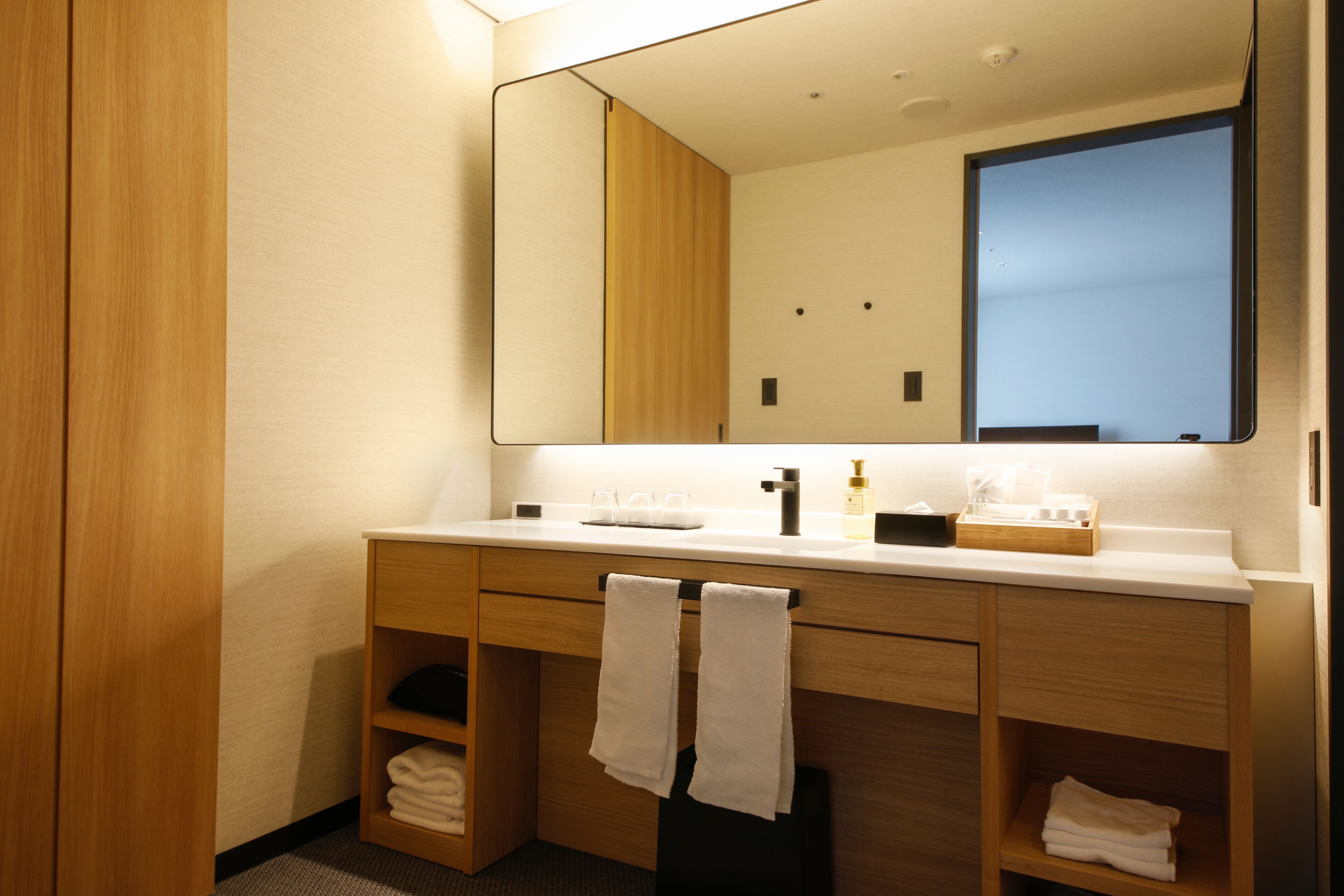 Un baño moderno con tocador de madera, un espejo grande y toallas ordenadamente dobladas.