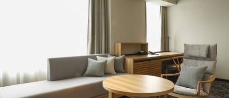Una habitación de hotel moderna con sofá, escritorio, silla y una mesa redonda.
