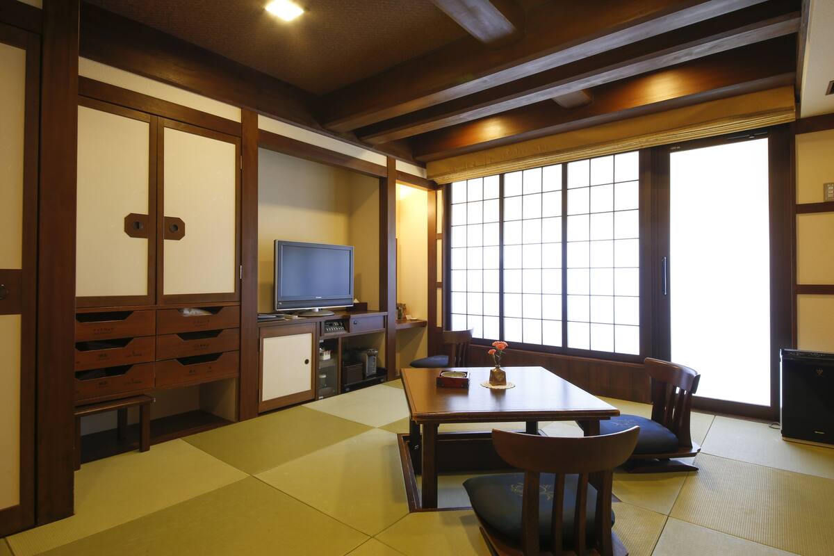 A traditional Japanese room with tatami flooring, a low table with cushions, a television, and sliding doors.