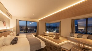 Una habitación de hotel moderna con una cama grande, un área de descanso con una mesa y ventanas amplias con vistas a la ciudad.