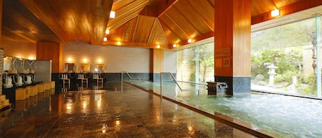 Un espacio interior amplio con piso de piedra pulida, techo de madera y grandes ventanales que dan a la naturaleza.