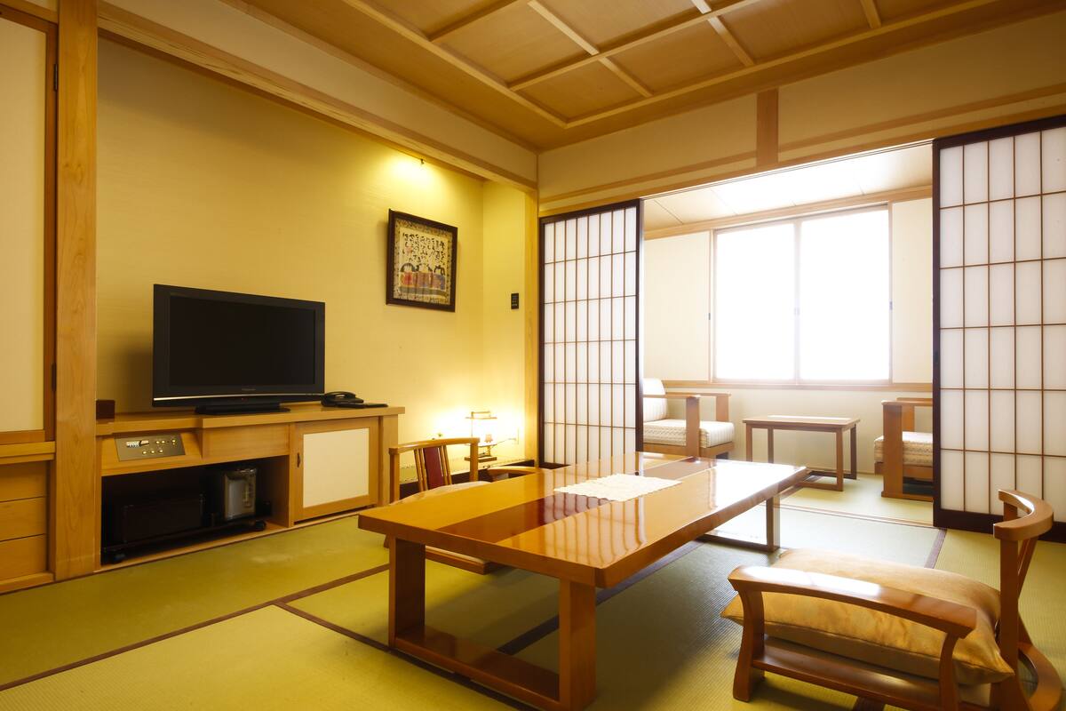 A traditional Japanese room with tatami flooring, a low wooden table, a television, and sliding shoji doors.