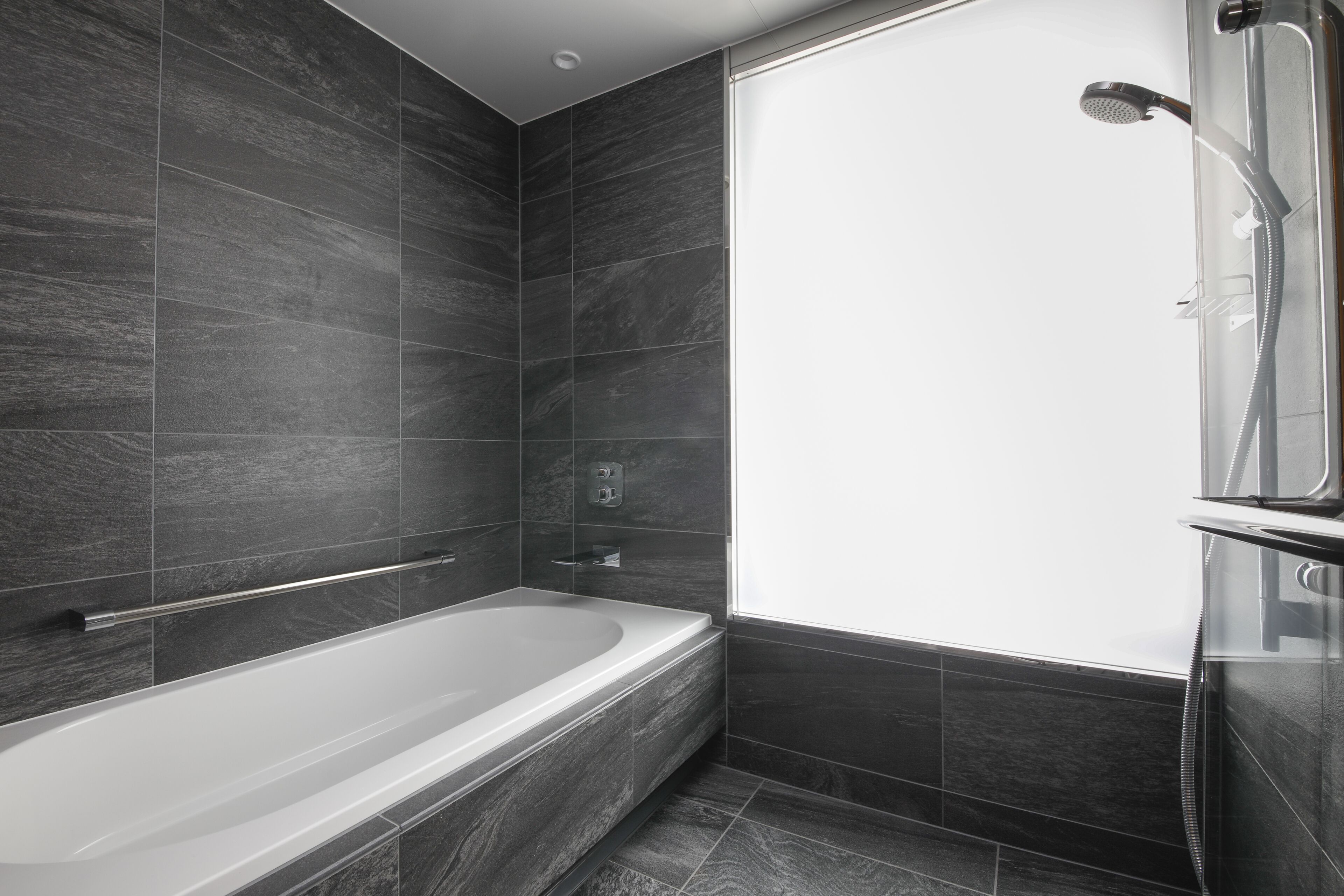 A modern bathroom with a freestanding bathtub, a shower area, and dark tiled walls.