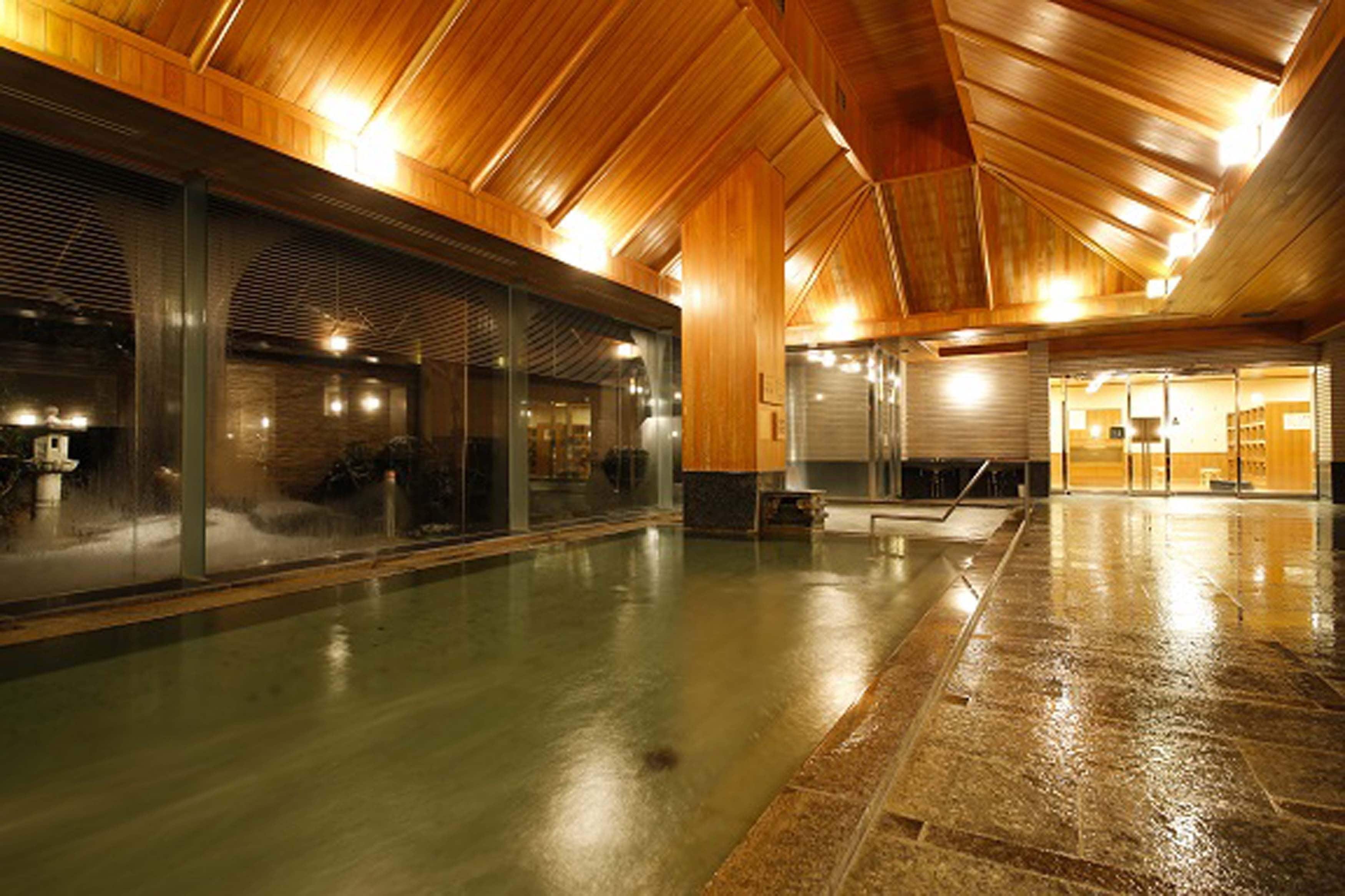 A spacious indoor swimming pool with a wooden ceiling and glass walls.