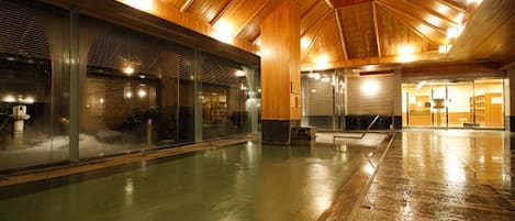 Una piscina interior amplia con techo de madera y paredes de vidrio.
