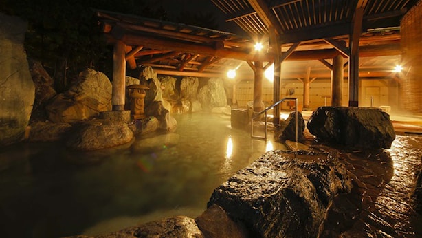 Un onsen japonés tradicional con estructura de madera, baños termales y grandes rocas.