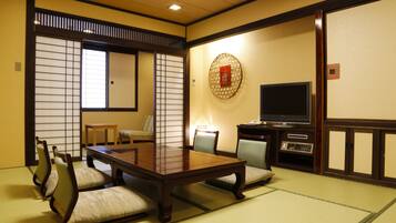 A traditional Japanese room with tatami flooring, a low table with cushions, a television, and a decorative wall hanging.