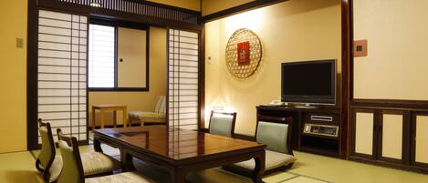 A traditional Japanese room with tatami flooring, a low table with cushions, a television, and a decorative wall hanging.