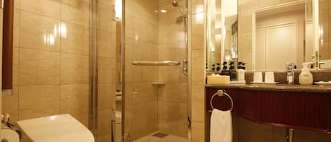 Un baño moderno con ducha envuelta en vidrio, inodoro blanco y tocador con artículos de aseo.