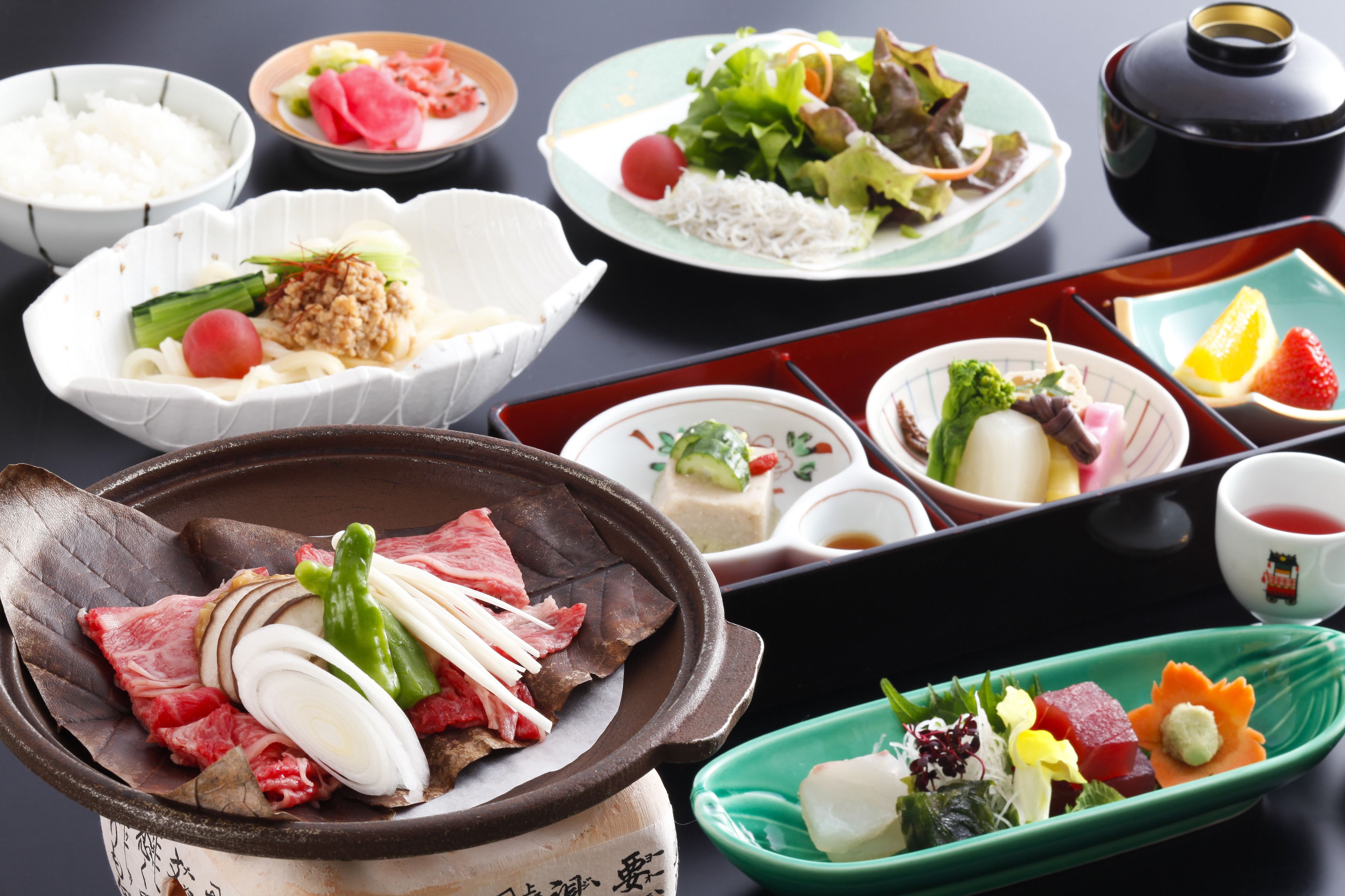 A variety of dishes including a bowl of rice, a plate with vegetables and meat, and a small dish with a green vegetable.