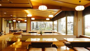 Un restaurante con mesas y bancos de madera, ventanas amplias y lámparas colgantes.