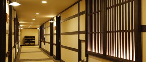 Un pasillo con esteras de tatami, puertas correderas tradicionales e iluminación empotrada.