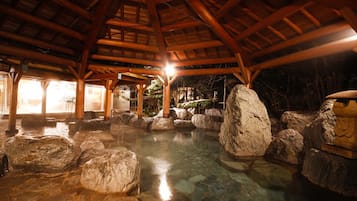 A hot spring area with large rocks and a wooden roof structure.