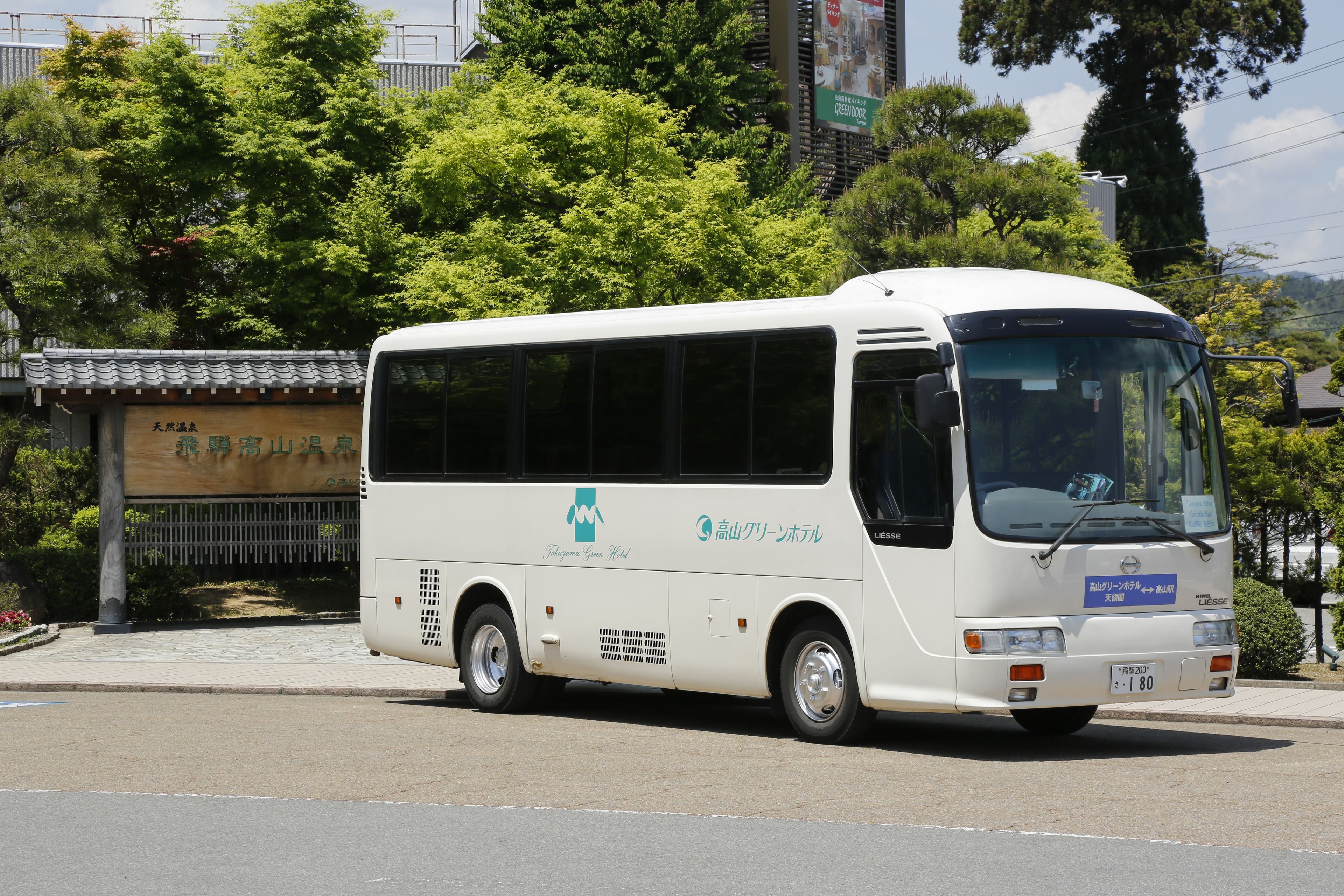 Un autobus blanc, orné d’un logo bleu et d’une inscription sur le côté, est garé dans une rue bordée d’arbres, avec un bâtiment visible au loin.
