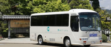 Een witte bus met een blauw logo en tekst op de zijkant, geparkeerd op een straat met bomen en een gebouw op de achtergrond.