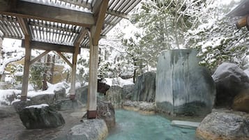 Un área de aguas termales naturales con piedras, una pérgola de madera y una piscina cristalina.