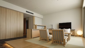 Una habitación de hotel moderna con piso de madera, un conjunto de sofá, un televisor de pantalla plana y una mesita de noche con lámpara.