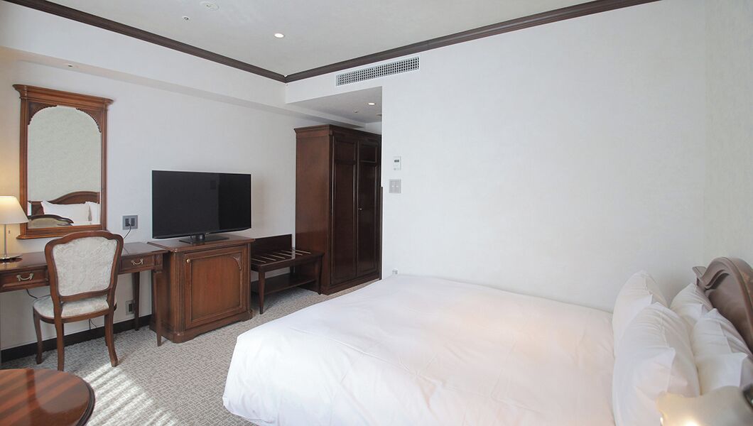 A hotel room with a bed, a desk with a television, a wardrobe, and a chair.
