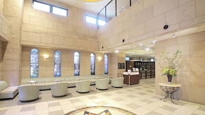 A spacious lobby with high ceilings, a seating area with cushioned benches, a reception desk, and a decorative vase with flowers. - Hotel Piena Kobe (Kobe)