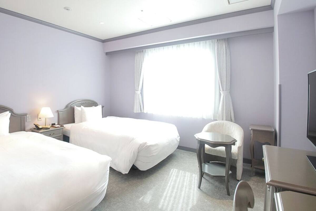 A hotel room with two beds, a desk, a chair, a TV, and a window with curtains.