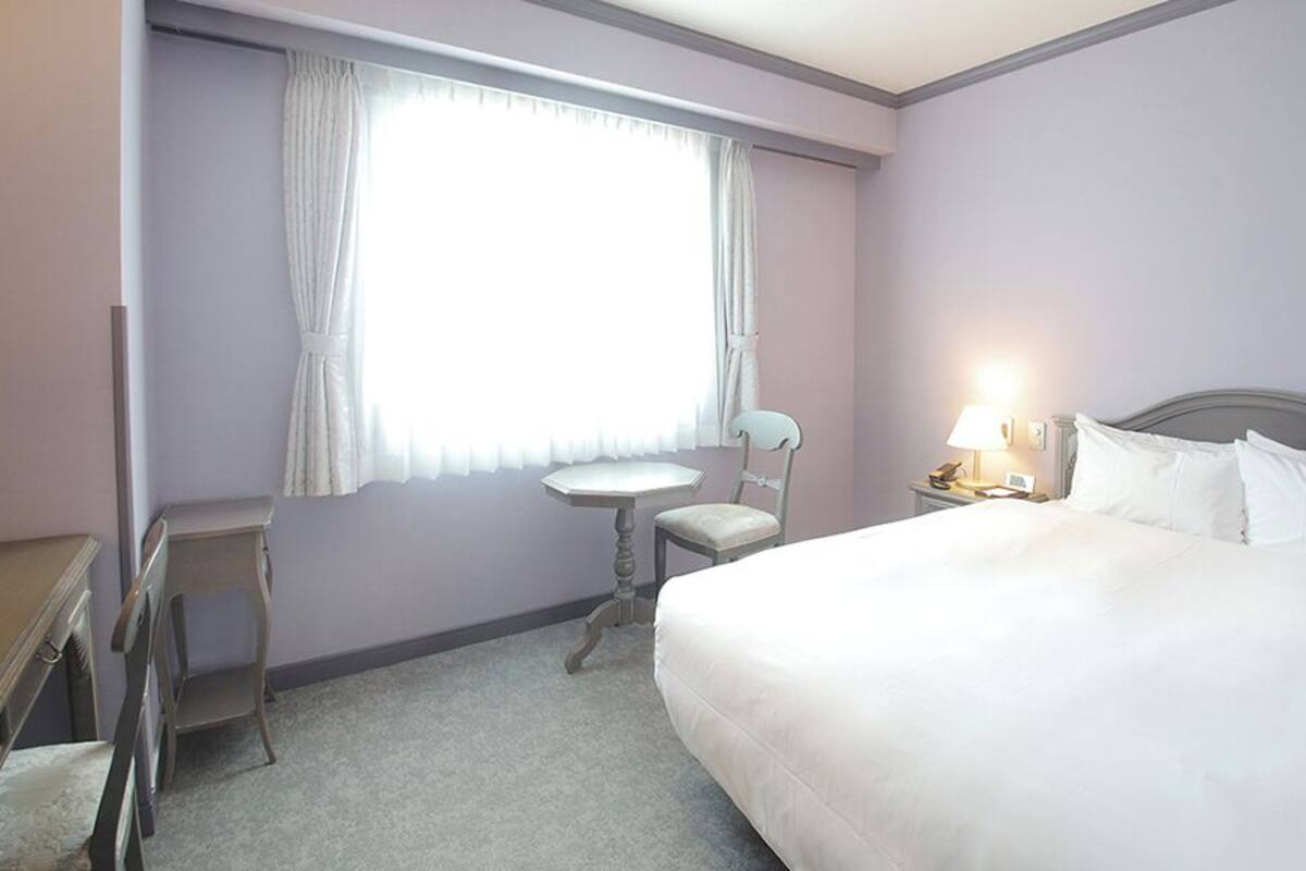 A hotel room with a bed, a desk, a chair, and a window with curtains.