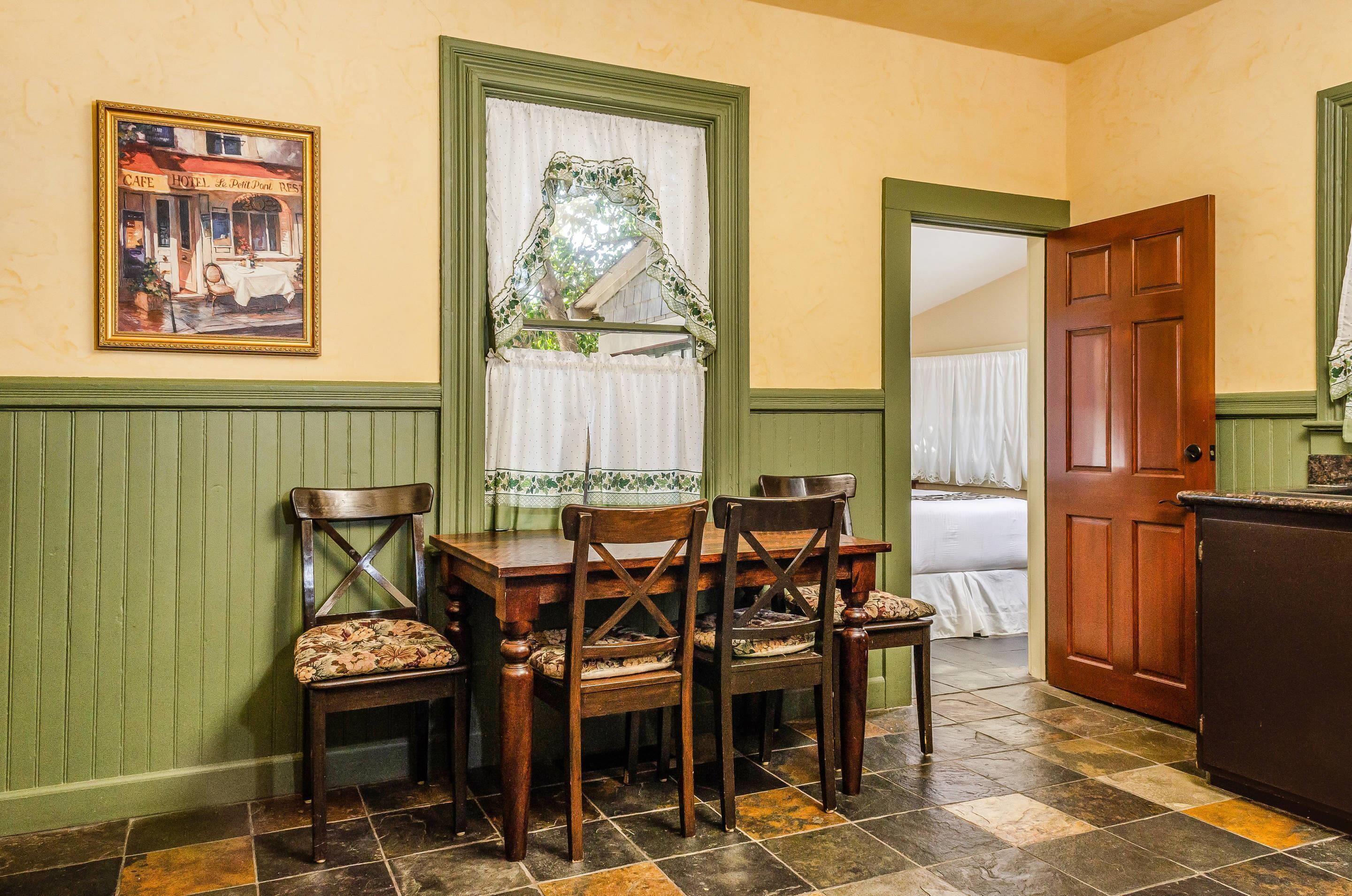 A dining area with a table and chairs, a window with curtains, and a door leading to another room.