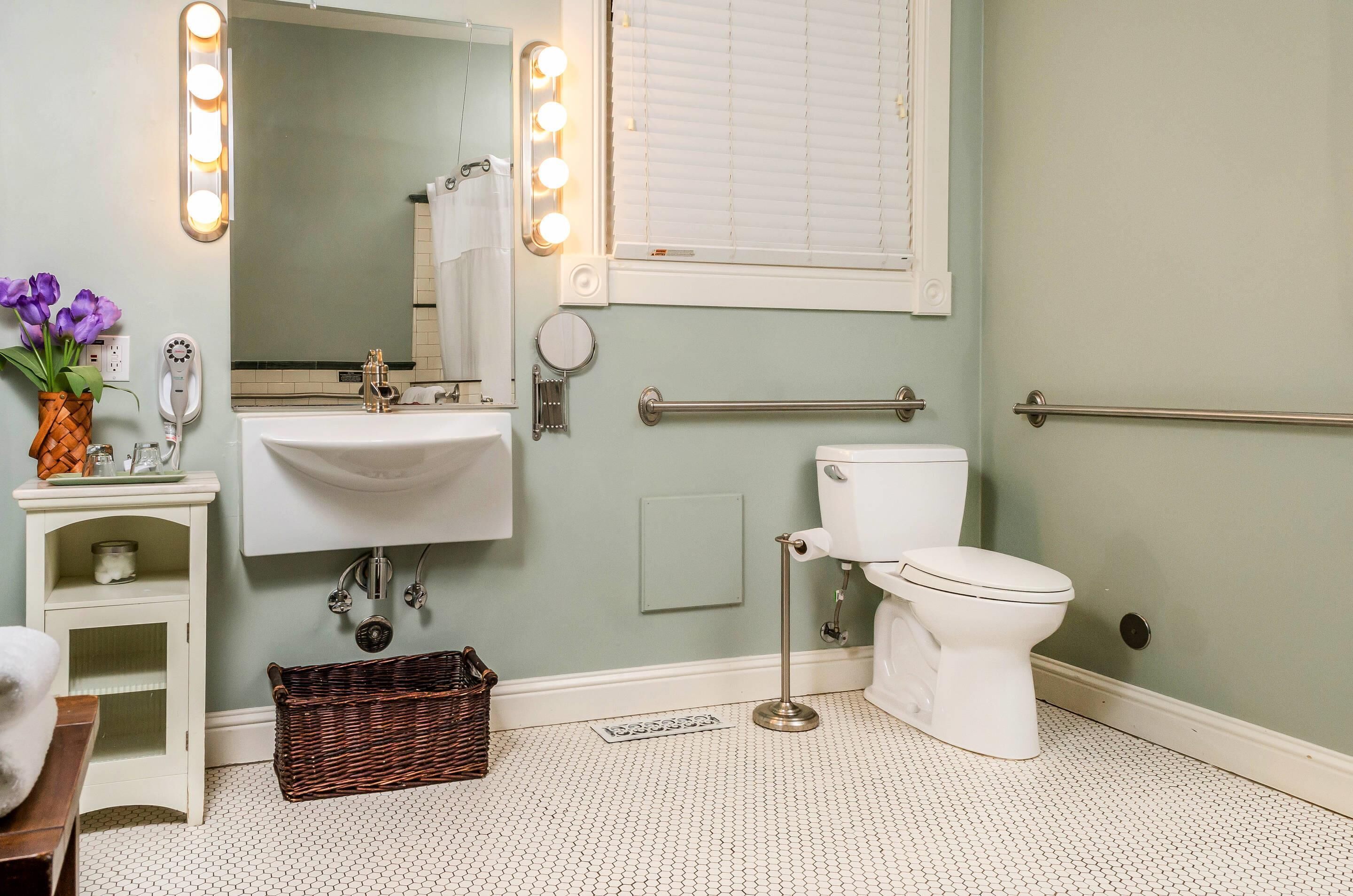 A bathroom with a sink, mirror, vanity, toilet, and a window with blinds.