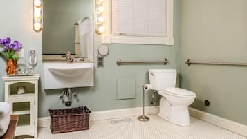 A bathroom with a sink, mirror, vanity, toilet, and a window with blinds.